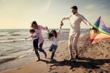 Çocukları dinlenen ve sonbahar günü filtresi boyunca sahilde uçurtmayla eğlenen genç bir aile.