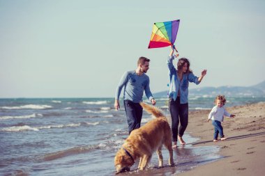 Mutlu ve çocuklu bir aile sonbahar günü filtresi boyunca sahilde köpek ve uçurtmayla eğleniyor.
