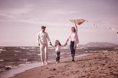 Çocukları dinlenen ve sonbahar günü filtresi boyunca sahilde uçurtmayla eğlenen genç bir aile.