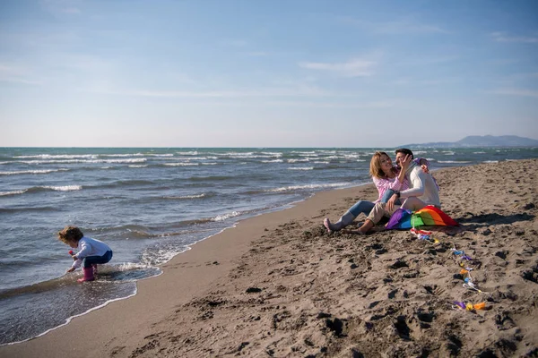 秋の日にビーチで石鹸バブルを作ることを楽しんでいる小さな娘を持つ家族 — ストック写真