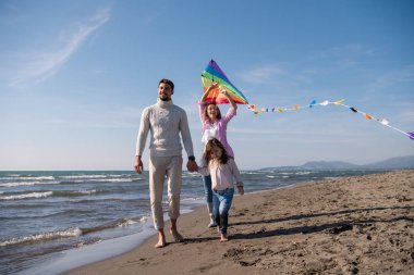 Genç bir aile, çocukları dinleniyor ve sonbahar günü kumsalda uçurtmayla eğleniyorlar.