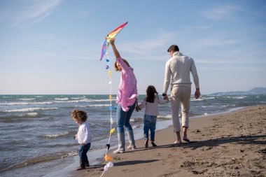 Genç bir aile, çocukları dinleniyor ve sonbahar günü kumsalda uçurtmayla eğleniyorlar.