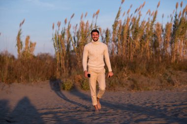 Kumsaldaki genç adam. Sıcak sonbahar gününün tadını çıkaran adam. Suyun yanında insan portresi