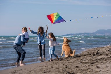Mutlu ve çocuklu bir aile sonbahar günü sahilde köpek ve uçurtmayla eğleniyor.