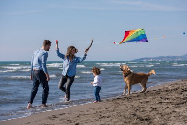Mutlu ve çocuklu bir aile sonbahar günü sahilde köpek ve uçurtmayla eğleniyor.