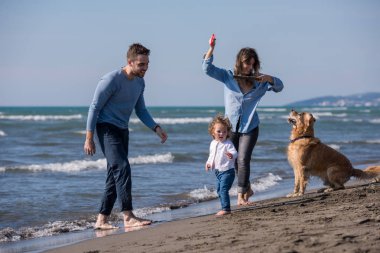 Mutlu ve çocuklu bir aile sonbahar günü sahilde köpek ve uçurtmayla eğleniyor.