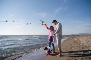 Genç bir aile, çocukları dinleniyor ve sonbahar günü kumsalda uçurtmayla eğleniyorlar.
