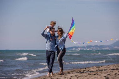 Genç bir aile, çocukları dinleniyor ve sonbahar günü kumsalda uçurtmayla eğleniyorlar.