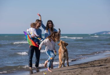 Mutlu ve çocuklu bir aile sonbahar günü sahilde köpek ve uçurtmayla eğleniyor.