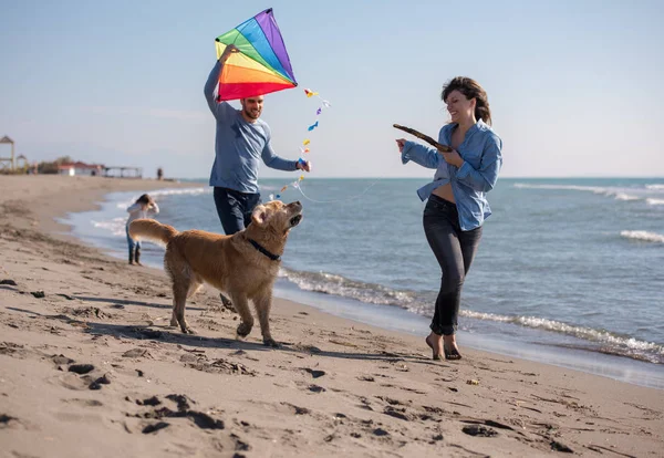 秋の日にビーチで犬と凧を楽しんでいる子供たちと幸せな若い家族 — ストック写真