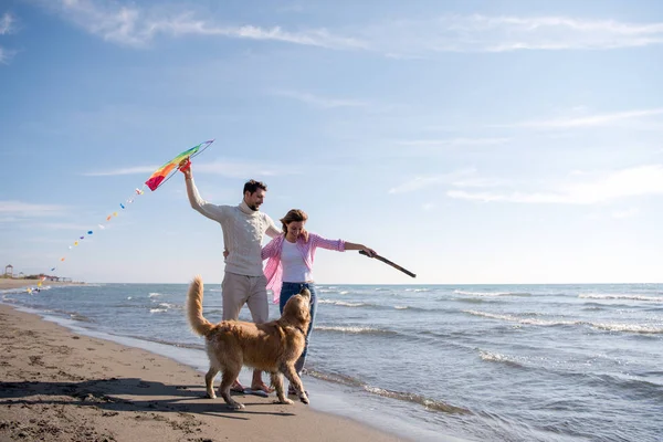 若いカップルが楽しんで犬 秋の日にビーチにカイトで遊んで — ストック写真