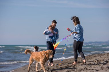 Mutlu ve çocuklu bir aile sonbahar günü sahilde köpek ve uçurtmayla eğleniyor.