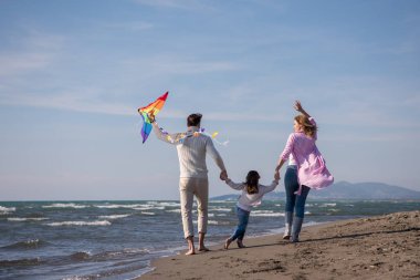 Genç bir aile, çocukları dinleniyor ve sonbahar günü kumsalda uçurtmayla eğleniyorlar.