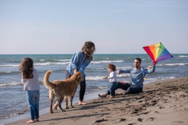 Mutlu ve çocuklu bir aile sonbahar günü sahilde köpek ve uçurtmayla eğleniyor.