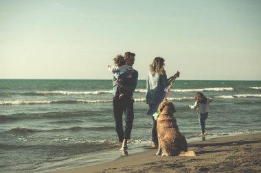 Mutlu ve çocuklu bir aile sonbahar günü filtresi boyunca sahilde köpek ve uçurtmayla eğleniyor.