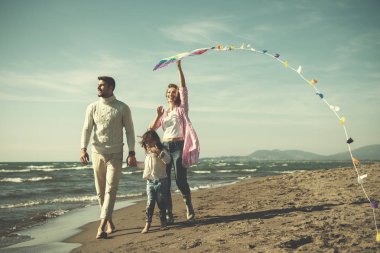 Çocukları dinlenen ve sonbahar günü filtresi boyunca sahilde uçurtmayla eğlenen genç bir aile.