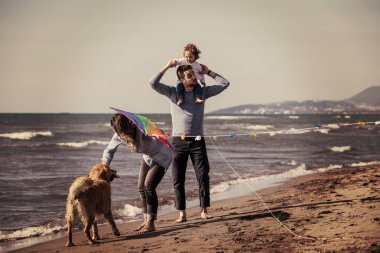 Mutlu ve çocuklu bir aile sonbahar günü filtresi boyunca sahilde köpek ve uçurtmayla eğleniyor.
