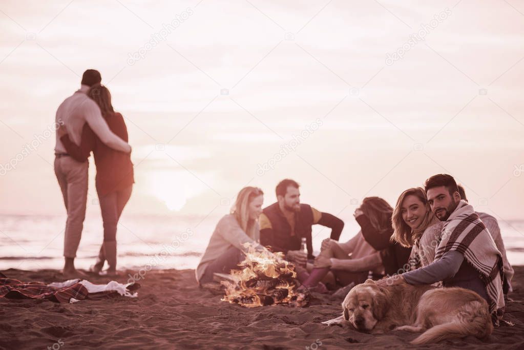 Young Couple enjoying with friends Around Campfire on The Beach At sunset drinking beer filter