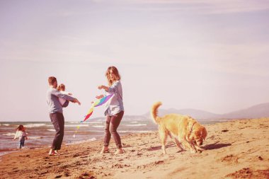 Mutlu ve çocuklu bir aile sonbahar günü filtresi boyunca sahilde köpek ve uçurtmayla eğleniyor.
