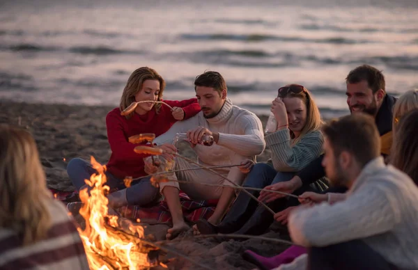 Grupo Jóvenes Amigos Sentados Junto Fuego Playa Otoño Asando Salchichas —  Fotos de Stock