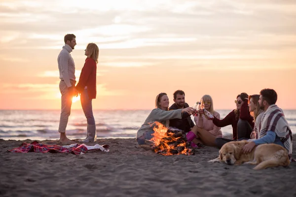Genç Çift Gün Batımında Arkadaşlarıyla Kumsaldaki Kamp Ateşinde Bira Içerek — Stok fotoğraf