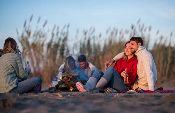 Young Couple enjoying with friends Around Campfire on The Beach At sunset drinking beer