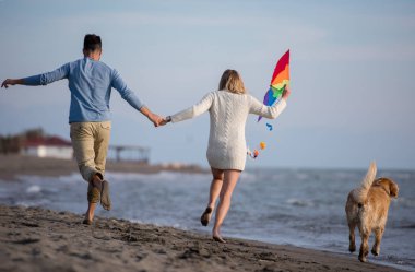 Genç çift eğlenmek bir köpek ve sonbahar günü plaj uçurtma ile oynarken