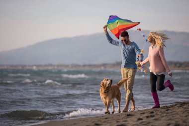 Genç çift eğlenmek bir köpek ve sonbahar günü plaj uçurtma ile oynarken