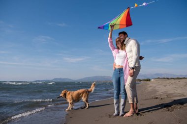 Genç çift eğlenmek bir köpek ve sonbahar günü plaj uçurtma ile oynarken
