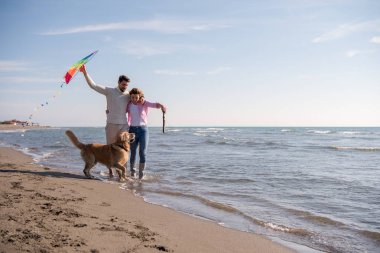 Genç çift eğlenmek bir köpek ve sonbahar günü plaj uçurtma ile oynarken