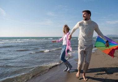 Genç çift sonbahar günü sahilde eğleniyor ve uçurtmayla oynuyor.