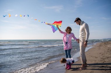 Genç bir aile, çocukları dinleniyor ve sonbahar günü kumsalda uçurtmayla eğleniyorlar.