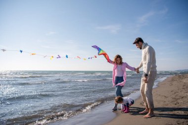 Genç bir aile, çocukları dinleniyor ve sonbahar günü kumsalda uçurtmayla eğleniyorlar.