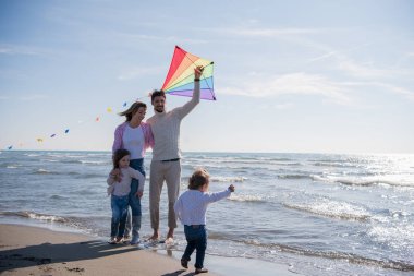 Genç bir aile, çocukları dinleniyor ve sonbahar günü kumsalda uçurtmayla eğleniyorlar.