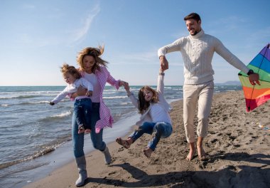 Genç bir aile, çocukları dinleniyor ve sonbahar günü kumsalda uçurtmayla eğleniyorlar.