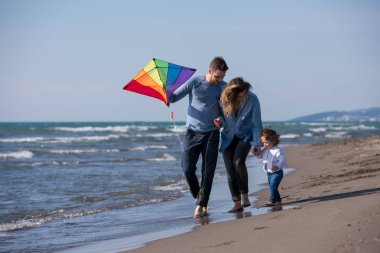 Genç bir aile, çocukları dinleniyor ve sonbahar günü kumsalda uçurtmayla eğleniyorlar.