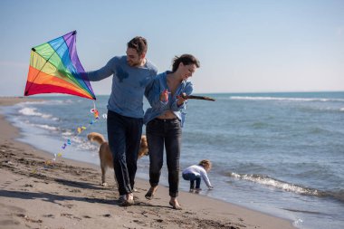 Mutlu ve çocuklu bir aile sonbahar günü sahilde köpek ve uçurtmayla eğleniyor.