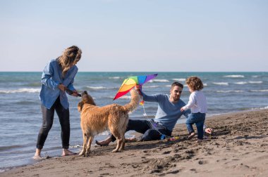 Mutlu ve çocuklu bir aile sonbahar günü sahilde köpek ve uçurtmayla eğleniyor.