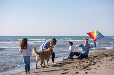 Mutlu ve çocuklu bir aile sonbahar günü sahilde köpek ve uçurtmayla eğleniyor.