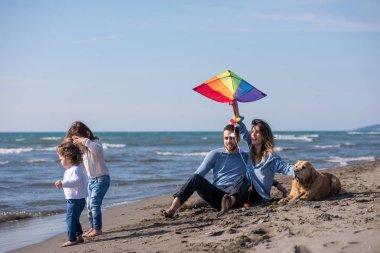Mutlu ve çocuklu bir aile sonbahar günü sahilde köpek ve uçurtmayla eğleniyor.