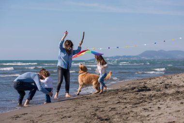 Mutlu ve çocuklu bir aile sonbahar günü sahilde köpek ve uçurtmayla eğleniyor.