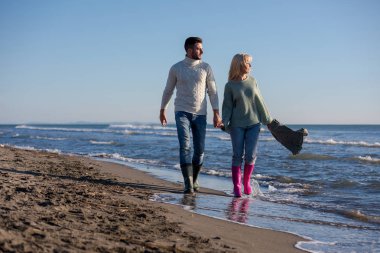 Genç çift, sonbahar güneşli bir günde kumsalda yürüyüp sarılıyor.