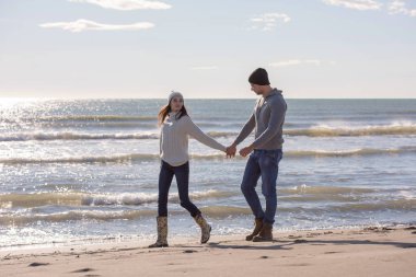 Genç çift, sonbahar güneşli bir günde kumsalda yürüyüp sarılıyor.