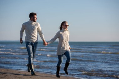 Genç çift, sonbahar güneşli bir günde kumsalda yürüyüp sarılıyor.