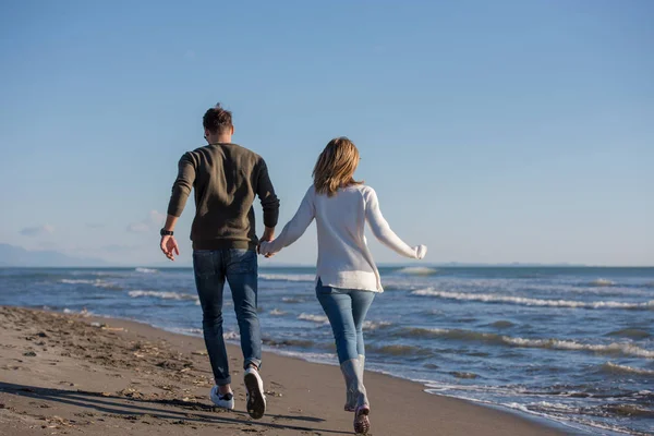 Genç çift, sonbahar güneşli bir günde kumsalda yürüyüp sarılıyor.