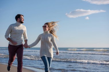 Genç çift, sonbahar güneşli bir günde kumsalda yürüyüp sarılıyor.