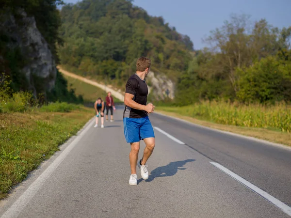 一群年轻人慢跑在乡间公路上跑步的人在一个夏日的道路上奔跑 — 图库照片