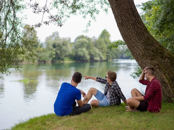 川の土手の上に座って自然を楽しんでいる若い男性のグループ — ストック写真