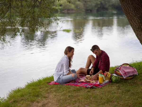 ピクニック時間飲み物と川の土手で美しい自然の食べ物を楽しんで愛のカップル — ストック写真