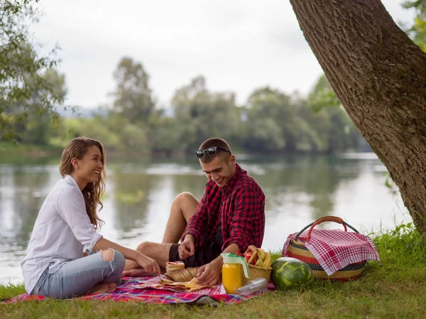 情侣在爱享受野餐时间饮料和食物在河岸边的美丽的自然 — 图库照片